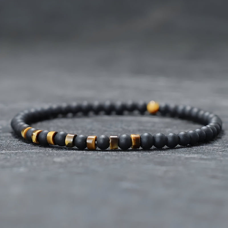 Bracelet fin pour homme en perles noires d'onyx avec accents métalliques et pierres jaunes œil de tigre.