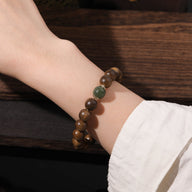 Bracelet marron en perles de bois d'agar et verre vert, fermoir doré délicat, style naturel et élégant.