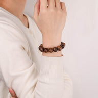 Bracelet en perles rondes en bois de rose marron foncé, porté au poignet, style classique et élégant.