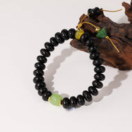 Bracelet femme en perles rondes noires de bois de santal avec deux perles de verre vertes et fermoir jaune.