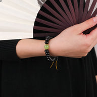 Bracelet femme en perles noires de bois de santal avec perle centrale verte et cordon ajustable jaune.