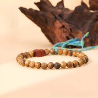 Bracelet en perles de bois de santal marron avec ornement floral en pierre rouge et cordon bleu ornant.