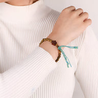 Bracelet marron en perles de bois de santal avec ornement floral vert et brins tressés turquoise.