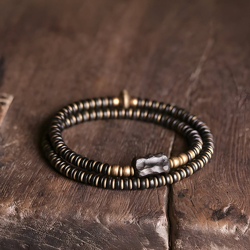 Bracelet double tour en perles de bois d’ébène noir et éléments en cuivre mat sur table en bois.