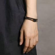 Bracelet double tour en perles de bois d’ébène noir et cuivre, style bohème chic, porté au poignet féminin.
