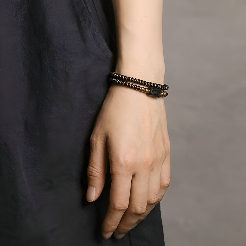 Bracelet double tour en perles de bois d’ébène noir et cuivre, style bohème chic, porté au poignet féminin.