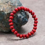 Bracelet mixte en perles de bois rouges lisses, cercle régulier posé sur pierre rugueuse grise.