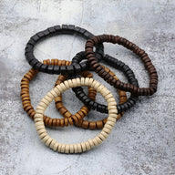 Bracelets en perles de bois naturels pour homme, couleurs noir, marron, café et beige sur fond gris béton.