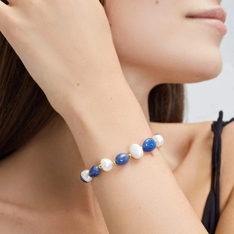 Bracelet ajustable en perles d'eau douce blanches et bleues sur chaîne dorée porté au poignet féminin.