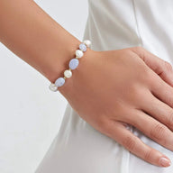 Bracelet ajustable en perles d'eau douce blanches et bleues avec petits noeuds dorés sur peau claire.