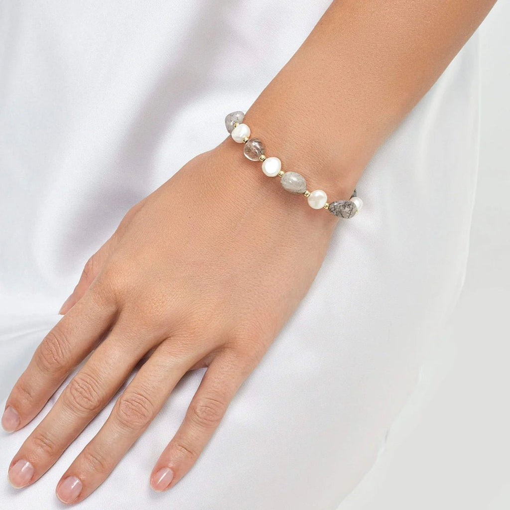 Bracelet ajustable en perles d'eau douce blanches avec petits détails argentés sur un poignet féminin.