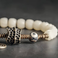 Bracelet femme perles blanches d'os de yak avec pendentif cuivre texturé et perle décorative noire et blanche.