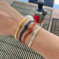 Bracelets en perles japonaises avec nœud central, coloris or, bleu, rouge et blanc sur poignet féminin.