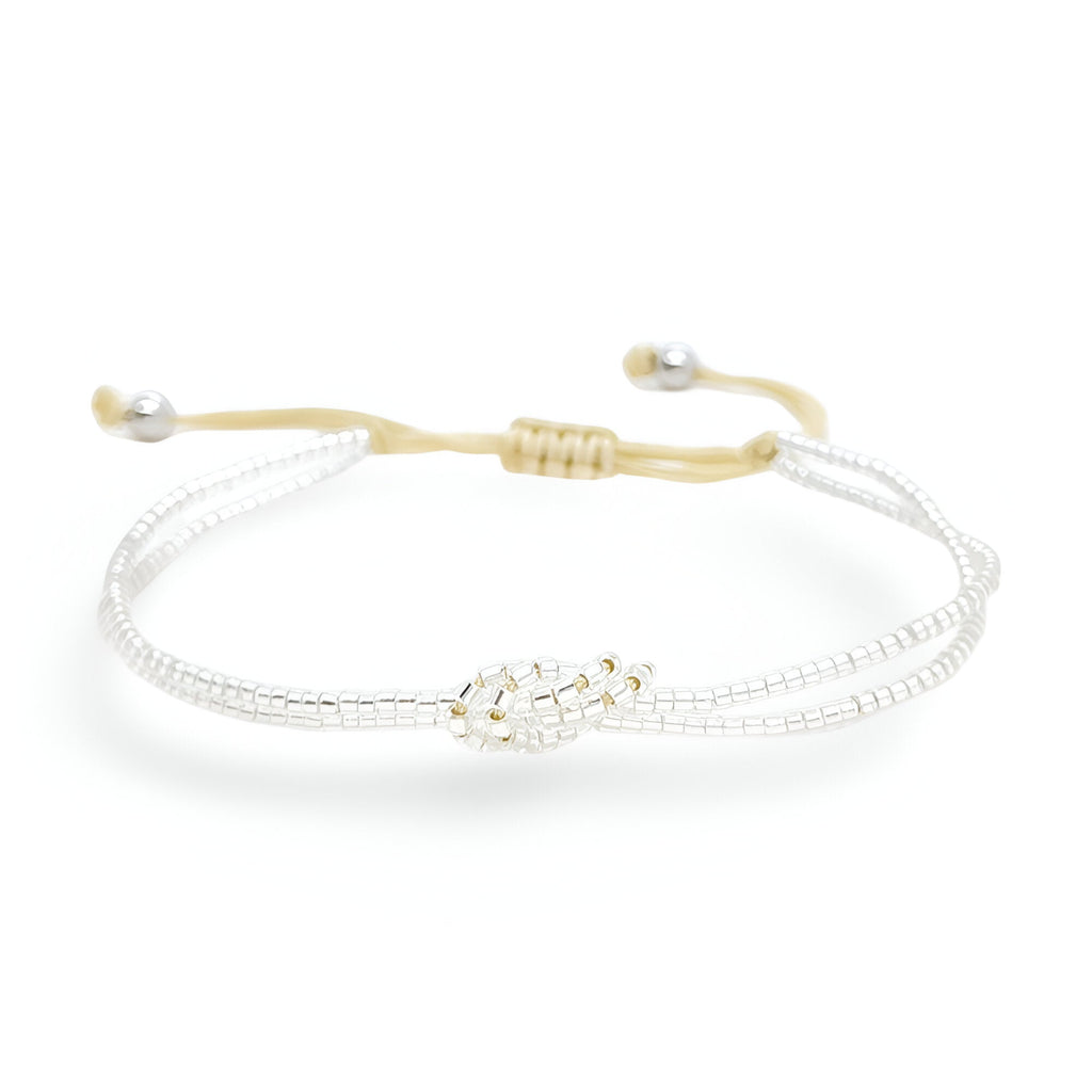 Bracelet femme perles blanches Japon avec nœud central doré et cordon ajustable beige.