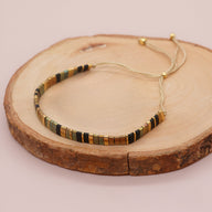 Bracelet ajustable en perles plates dorées, noires et marron, cordon beige délicat.