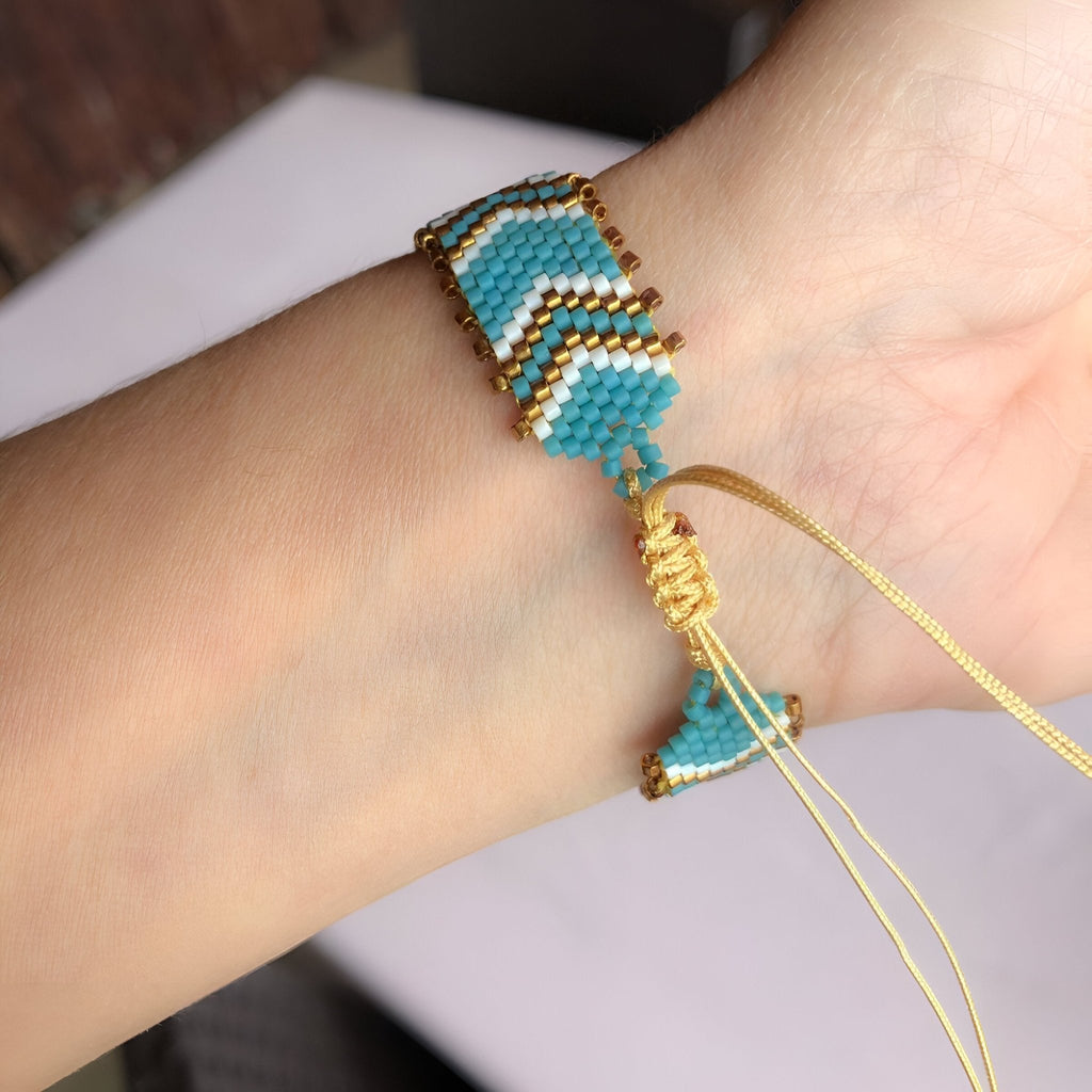 Bracelet ajustable en perles japonaises bleues, blanches et dorées, motif en chevrons sur poignet féminin.