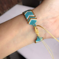 Bracelet ajustable en perles japonaises bleues, blanches et dorées, motif en chevrons sur poignet féminin.