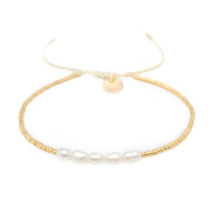 Bracelet fin en perles dorées avec six perles blanches ovales centrales et fermoir coulissant pigment crème.