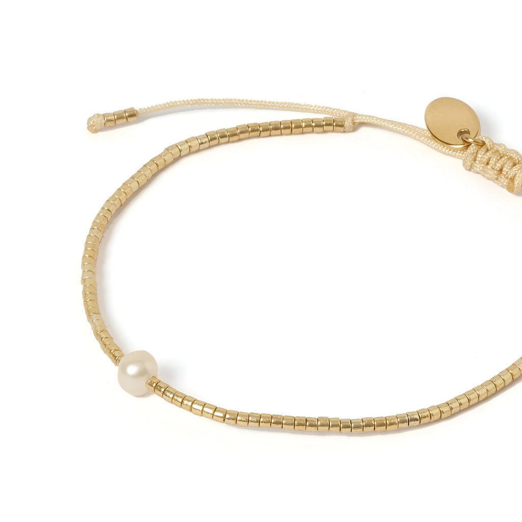 Bracelet fin en perles dorées du Japon avec une perle blanche centrale et fermoir coulissant beige.