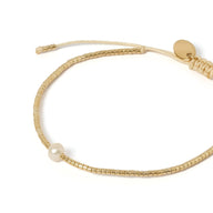 Bracelet fin en perles dorées du Japon avec une perle blanche centrale et fermoir coulissant beige.