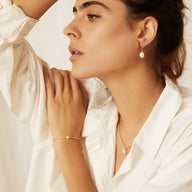 Bracelet fin en perles dorées du Japon porté avec une blouse blanche, style élégant féminin.