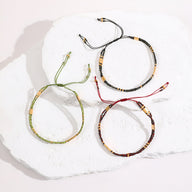 Trois bracelets double-rangs en perles du Japon, ajustables, en beige, vert et bordeaux, détails noirs et dorés.