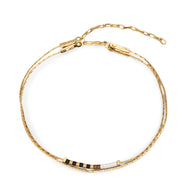 Bracelet double-rangs en perles noires et blanches avec chaîne fine dorée et fermoir élégant.