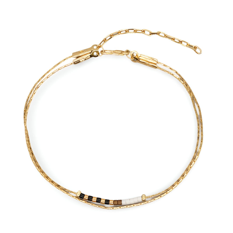 Bracelet double-rangs en perles noires et blanches avec chaîne fine dorée et fermoir élégant.