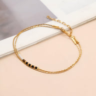 Bracelet double rangs en perles noires et dorées avec chaîne et fermoir doré élégant.