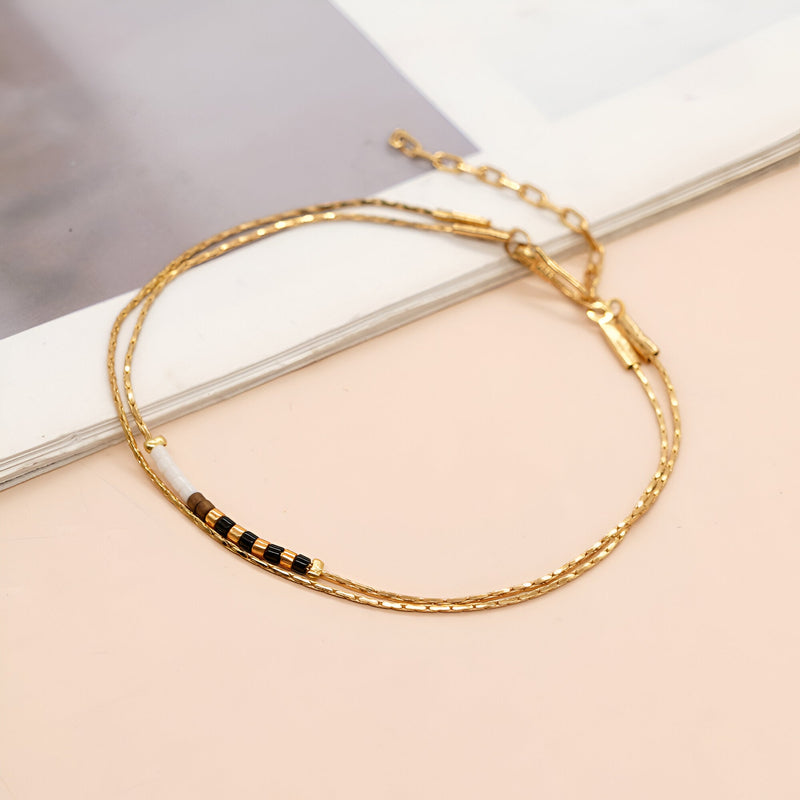 Bracelet double rangs en perles noires et dorées avec chaîne et fermoir doré élégant.