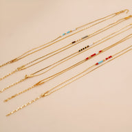 Bracelet double-rangs en perles rouges, bleues et blanches avec chaînes fines dorées.