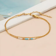 Bracelet double-rangs en perles bleu clair et blanches avec chaîne fine dorée et fermoir ajustable.