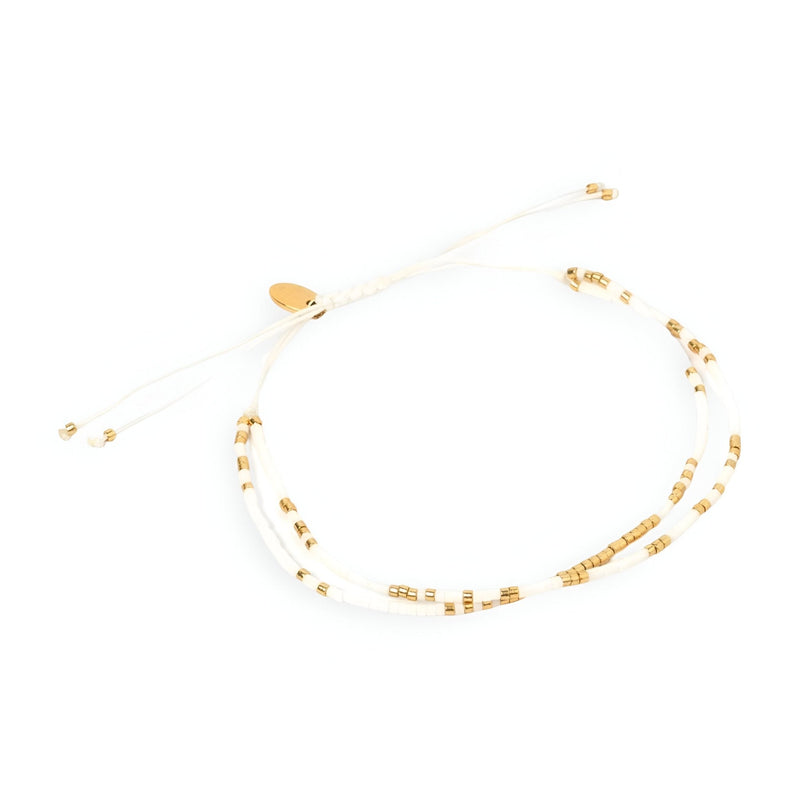Bracelet double rangs en perles blanches et dorées avec cordon ajustable et petits pompons.