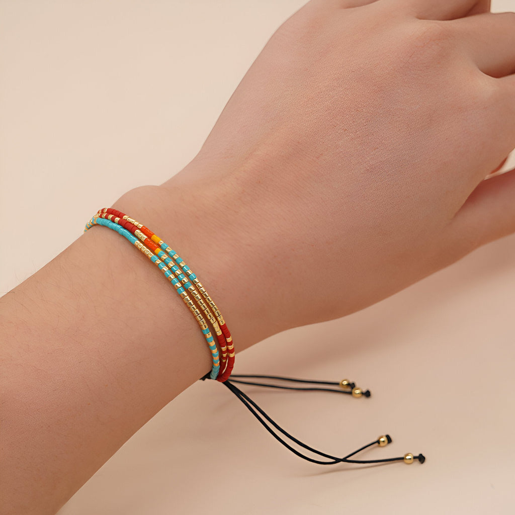 Bracelet multi-rangs pour femme en perles colorées rouge, bleu, blanc et or avec cordon noir et embouts dorés.