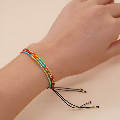 Bracelet multi-rangs pour femme en perles colorées rouge, bleu, blanc et or avec cordon noir et embouts dorés.