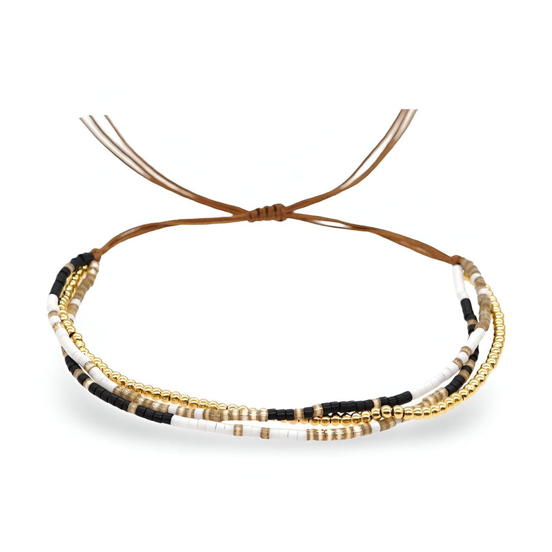 Bracelet multi-rangs avec perles blanches, noires et dorées sur cordon marron ajustable.