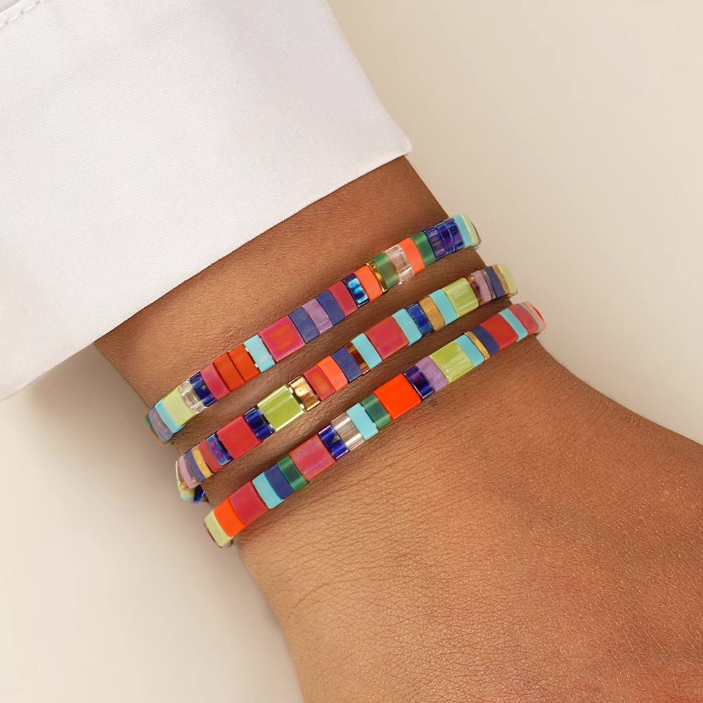 Bracelet femme en perles japonaises multicolores à motifs rayés avec petits carrés dorés.