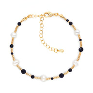 Bracelet fin en perles blanches et noires avec pierre de grès, fermoir doré ajustable.