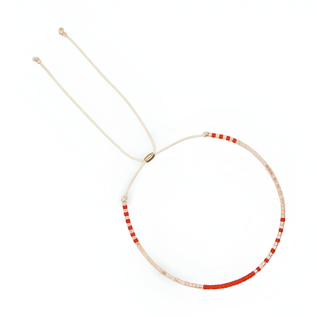 Bracelet fin en perles rouges et blanches avec cordon beige ajustable et embouts dorés.