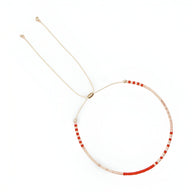 Bracelet fin en perles rouges et blanches avec cordon beige ajustable et embouts dorés.