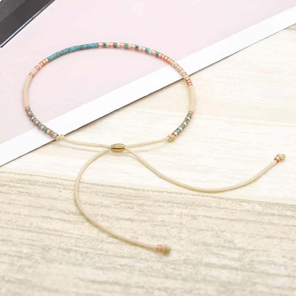 Bracelet fin avec perles turquoise et dorées, cordon beige ajustable en tissu doux.