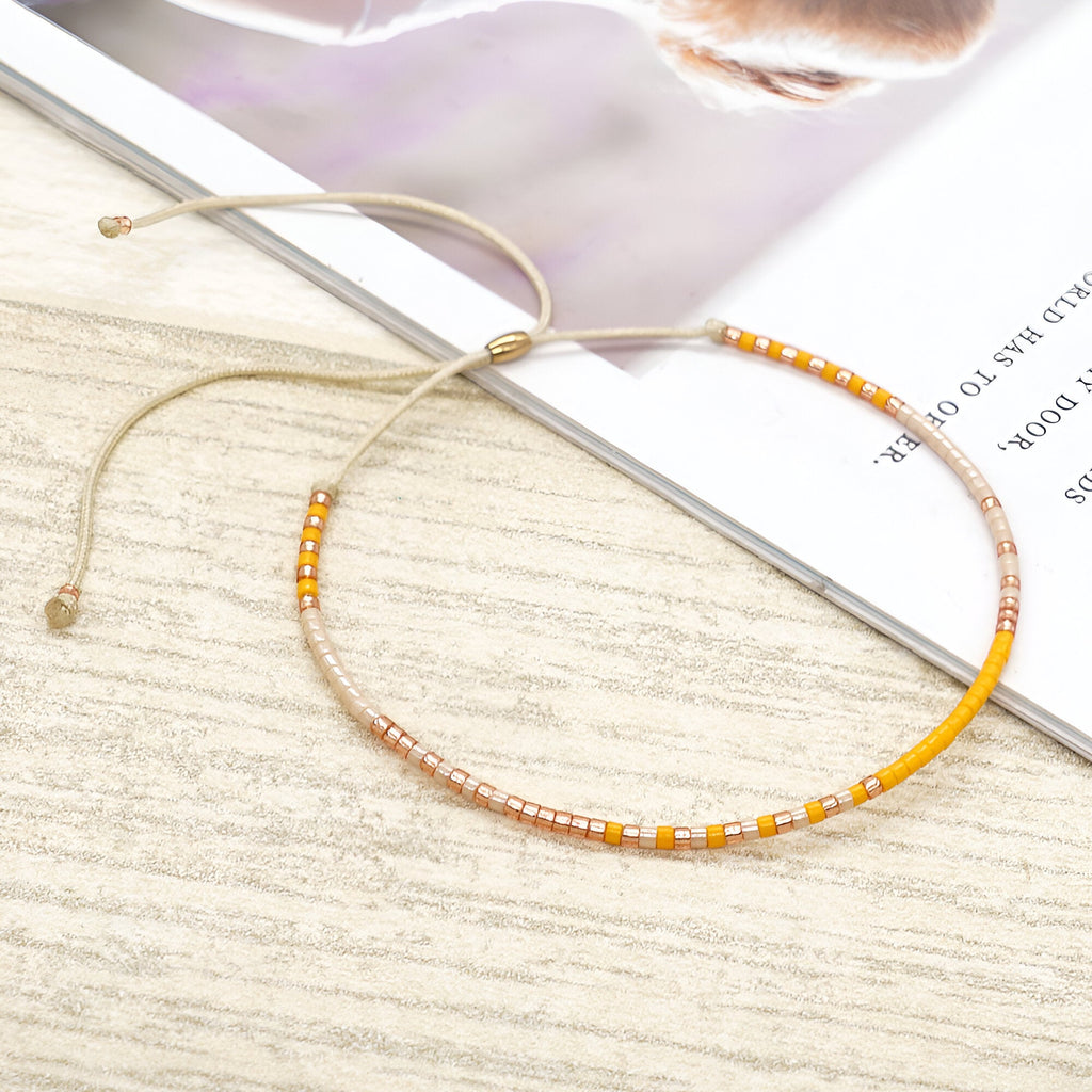 Bracelet fin en perles jaunes et blanches avec cordon ajustable beige sur fond clair.