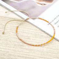 Bracelet fin en perles jaunes et blanches avec cordon ajustable beige sur fond clair.