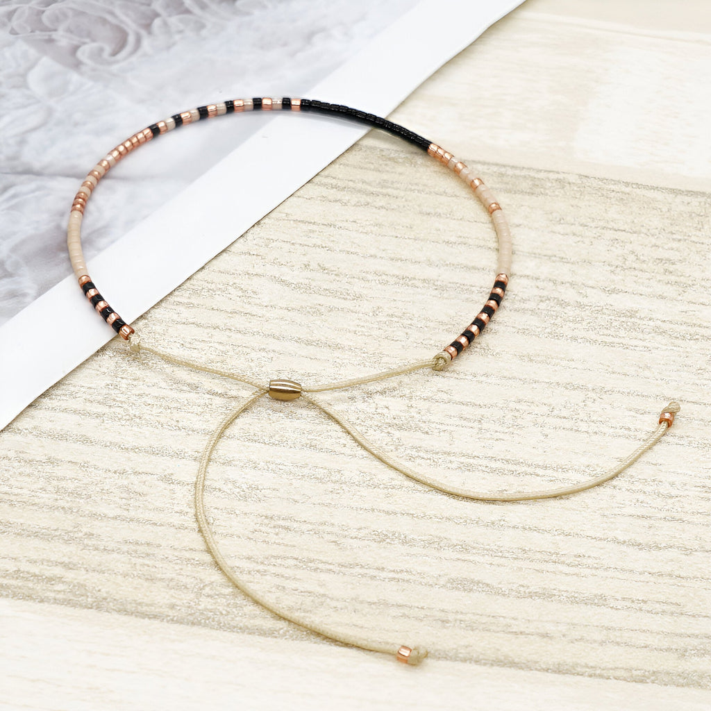 Bracelet fin en perles noires et dorées avec cordon réglable beige et fermoir doré.