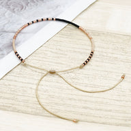 Bracelet fin en perles noires et dorées avec cordon réglable beige et fermoir doré.