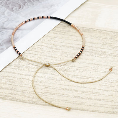 Bracelet fin en perles noires et dorées avec cordon réglable beige et fermoir doré.