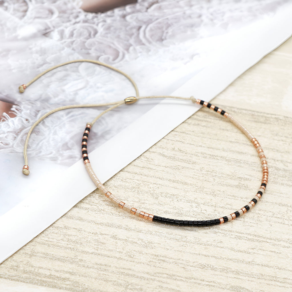Bracelet fin en perles noires et dorées, style minimaliste ajustable pour femme.