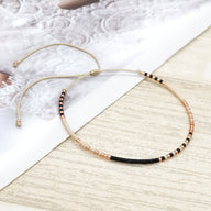 Bracelet fin en perles noires et dorées, style minimaliste ajustable pour femme.