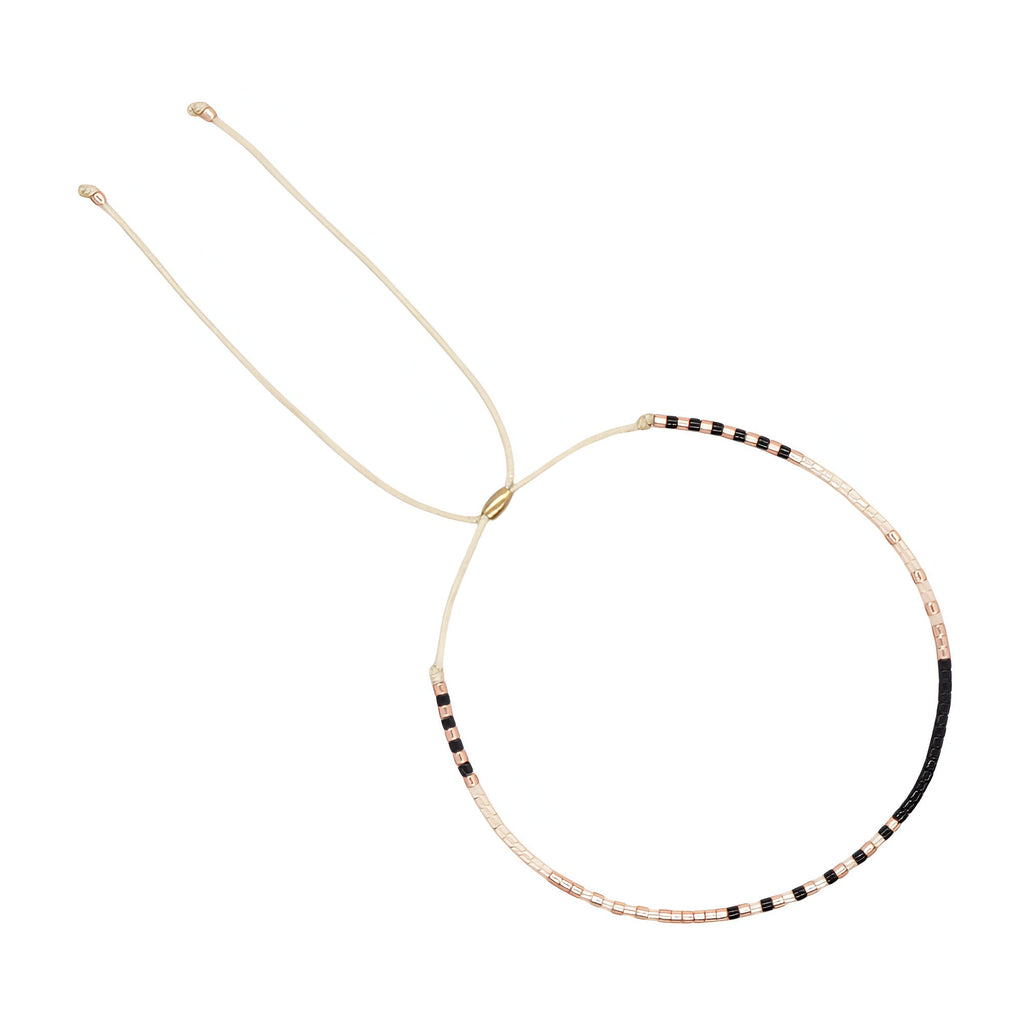 Bracelet fin à perles noires, beiges et blanches, réglable avec cordon beige léger.