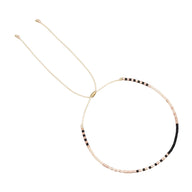 Bracelet fin à perles noires, beiges et blanches, réglable avec cordon beige léger.